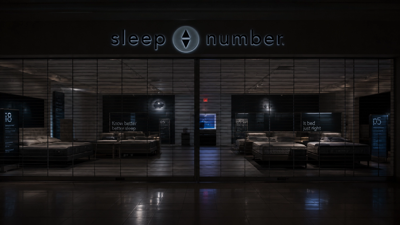 Closed mattress showroom with security gate pulled down and a red exit sign glowing inside